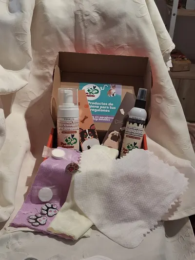 Foto sin retoque del pack para perros armado en su caja, con el champú seco, la loción con lanolina, toallas, separadores de libro, una chapita y aros con forma de huella